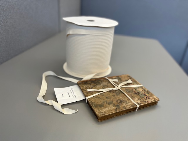 : Spool of binding tape alongside an Estray Book whose cover is held in place by binding tape.