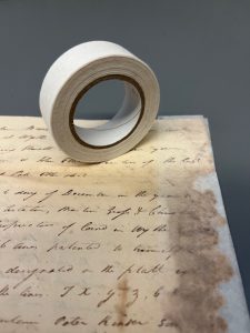 Heat-set Tissue: Roll of heat-set tissue alongside a document with fragile edges that an archivists stabilized using heat-set tissue